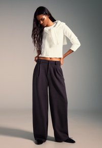 Biała prążkowana dzianinowa bluzka z kapturem i długimi rękawami; ciemne szerokie spodnie z przodu z zakładkami i bocznymi kieszeniami; czarne wsuwane buty.