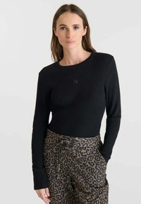 Pull noir à côtes avec des manches longues, un col rond et des poignets ajustés, associé à un pantalon à imprimé léopard avec une taille à cordon de serrage.