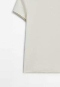 Haut à manches courtes en tissu côtelé couleur écru avec bordure beige aux extrémités des manches, présenté de la moitié du torse au haut du bras sur fond blanc.