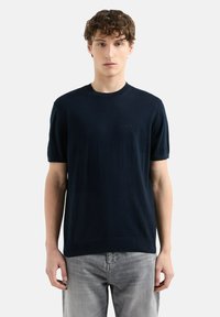 Pull à manches courtes bleu marine en tissu tricoté doux, avec un col rond et un discret logo sur la poitrine.