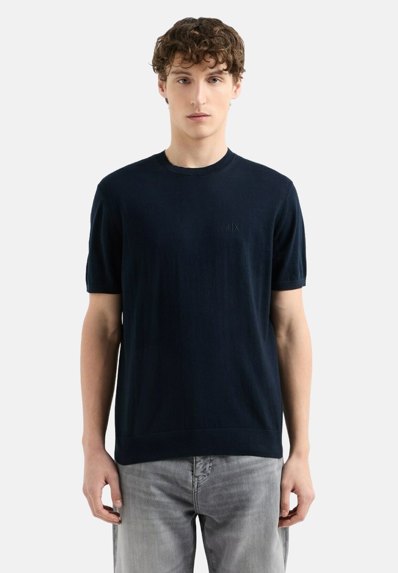 Pull à manches courtes bleu marine en tissu tricoté doux, avec un col rond et un discret logo sur la poitrine.