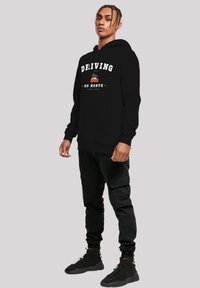 Black hooded sweatshirt with graphic text "DRIVING GO NORTH" and a car design. Features a kangaroo pocket and ribbed cuffs. Worn with black cargo pants.