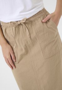 Jupe en coton beige avec taille élastique et cordon de serrage, dotée de deux poches latérales et d'une finition légèrement texturée.