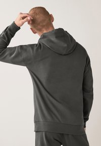 Dunkelgrauer Hoodie mit strukturiertem Finish, ausgestattet mit einer Kapuze mit Kordelzug und gerippten Bündchen. Das Design ist leicht locker geschnitten und betont den Komfort.