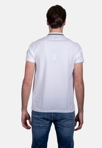Polo shirt bianco a maniche corte con colletto classico, texture liscia e rifiniture a contrasto intorno al colletto. Indossato con jeans blu.