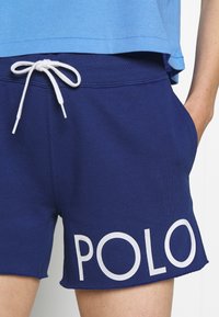 Námořnické modré bavlněné šortky s elastickým pasem na šňůrku, bočními kapsami a bílým nápisem "POLO" na levé nohavici.