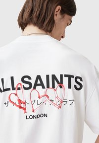 White cotton T-shirt featuring a bold black "ALLSAINTS" logo and three red outlined hearts on the back, with "LONDON" below the design.