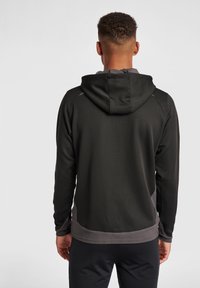 Felpa nera con finitura testurizzata e accenti grigi. Presenta un cappuccio, maniche lunghe e un design aderente. Materiale morbido, stile casual.