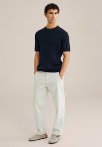 Jūros laivyno juostos mezgimo trumpomis rankovėmis megztinis, derinamas su šviesiai bežinėmis atsitiktinio stiliaus kelnėmis ir pilkiais batučiais. Paprastas dizainas su klasikine siluetu.