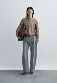 Striped brown and beige button-up shirt with a chest pocket, paired with light blue wide-leg jeans and a brown leather handbag.