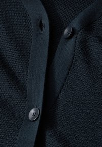 Mörkblå cardigan med texturerat stickat tyg, med knäppning fram och ett litet hål nära knäppningen.