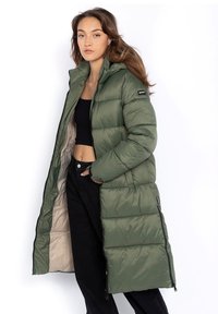 Grüner, gepolsterter, langer Mantel mit Kapuze, der einen Reißverschluss, seitliche Taschen und eine beigen Innenauskleidung aufweist. Der Stoff hat eine glatte Textur.