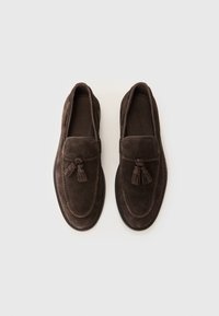 Mocassins en daim marron avec un bout rond, des coutures de mocassin et des glands décoratifs sur le dessus. Semelle en caoutchouc plate.