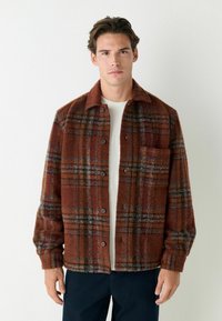 Plaid shirt jacket in warm brown tones with a textured surface. Features a button front, collar, and single chest pocket.