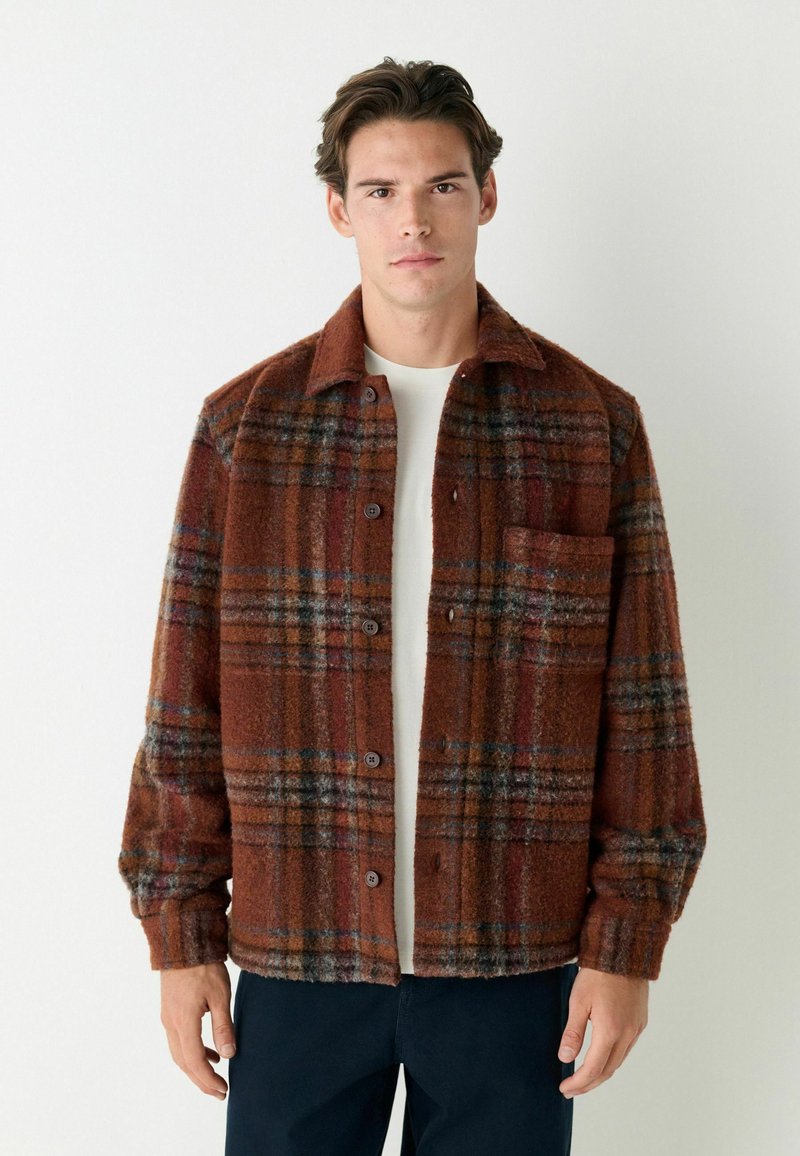 Plaid shirt jacket in warm brown tones with a textured surface. Features a button front, collar, and single chest pocket.