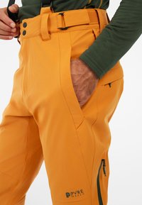 Oranje buitenbroeken met een rechte pasvorm, voorzien van een ritszak, knoopsluiting, verstelbare bandjes en "PYRE GREEN" branding.