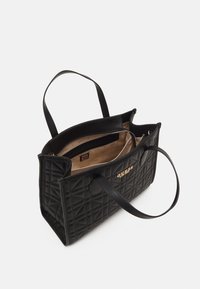 Sac fourre-tout noir matelassé avec des anses doubles, une poche zippée intérieure et une doublure crème avec un logo de marque subtil.