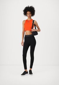 Débardeur court orange vif avec texture côtelée, associé à un legging noir taille haute et des baskets noires avec des semelles blanches.