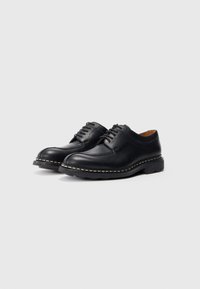 Schwarze Lederschuhe mit glatter Oberfläche, runder Zehenform, Schnürdesign und kontrastierendem weißen Nähten entlang der Sohle. Niedriger Absatz.