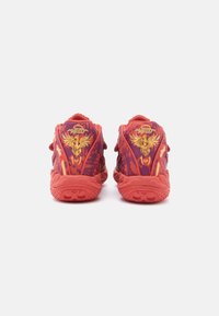 Czerwone buty sportowe z teksturowanym wzorem, z fioletowym i pomarańczowym motywem oraz złotymi akcentami na pięcie i bokach.