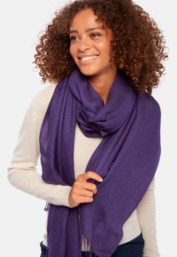Écharpe violette en tissu léger et texturé, drapée sur les épaules avec des extrémités à franges, renforçant son apparence douce.