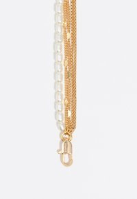 Collar en capas que presenta cadenas de oro y perlas blancas, con un detalle de cierre. El diseño combina diferentes texturas y formas para un interés visual.