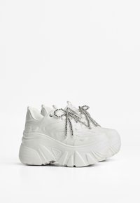 Vita sneakers med en kraftig plattform, texturerad ovandel och metalliska snören. Har en rund tå och en dragflik på hälen.