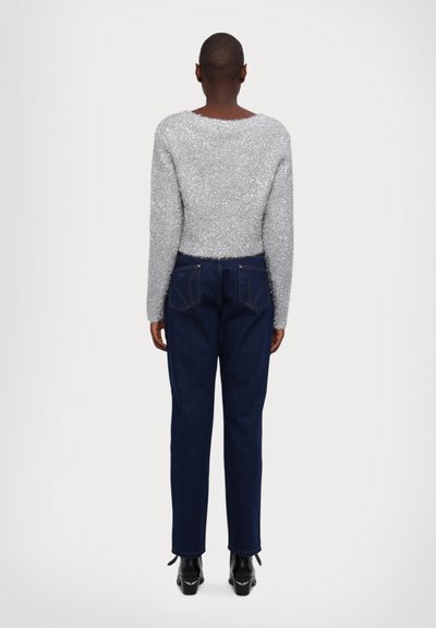Sølv, glitrende genser med lange ermer, kombinert med mørk denim jeans med baklommer. Modellen har på seg svarte støvler med hæl.