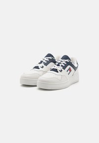 Sneakers bianchi in pelle con dettagli blu navy, suola spessa, punta tonda, dettagli perforati e logo sul lato. Chiusura con lacci.