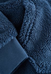 Blue fleece fabric with a soft, textured surface; ribbed cuffs in matching color; slightly wrinkled appearance emphasizes thickness and warmth.