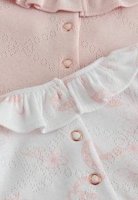 Primo piano di abbigliamento per neonati rosa e bianco con bottoni a pressione color oro rosa, caratterizzato da motivi lavorati a maglia a foro e un colletto arricciato sul capo bianco.