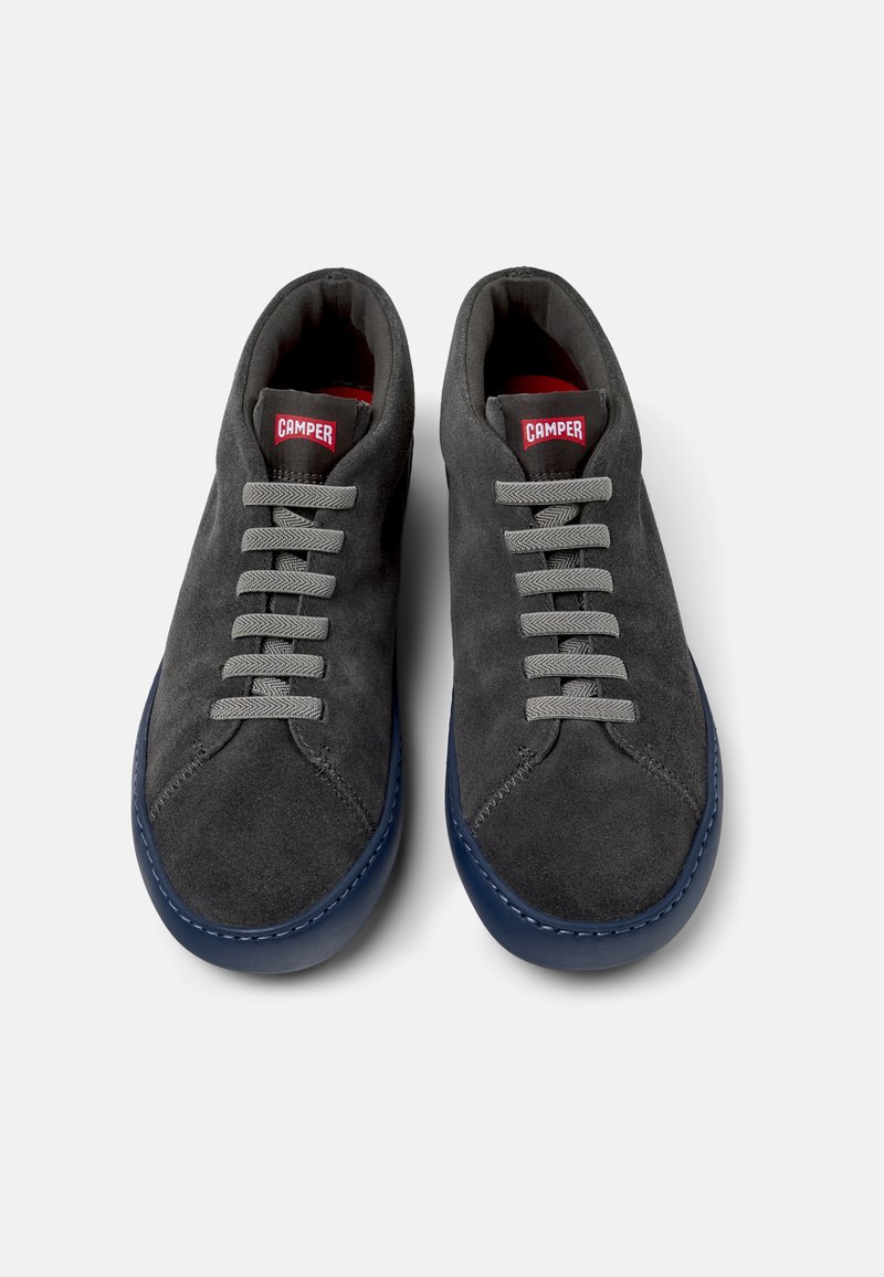 Graue Wildlederschuhe mit grauen Schnürsenkeln und einer blauen Sohle, mit einem roten "Camper"-Logo auf der Zunge, von oben vor einem weißen Hintergrund präsentiert.