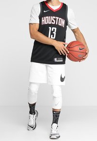 Czarna koszulka do koszykówki z napisem "HOUSTON" i numerem "13" w białym i czerwonym kolorze. Białe spodenki z logo Nike, podkolanówki w czarno-białe paski oraz piłka do koszykówki.