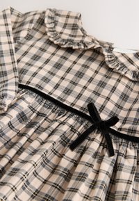 Plaid dress with a ruffled collar, beige, blue, and black colors. Features black velvet accents and gathered waist for a textured look.