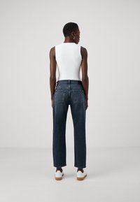 Jean foncé à taille haute, coupe droite, et poches arrière classiques, associé à un haut sans manches blanc et des baskets blanches.