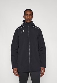 Μαύρο μπουφάν με κουκούλα από αδιάβροχο υλικό, με λευκές διακοσμητικές γραμμές, εμπρόσθιο φερμουάρ και λογότυπο στο στήθος.