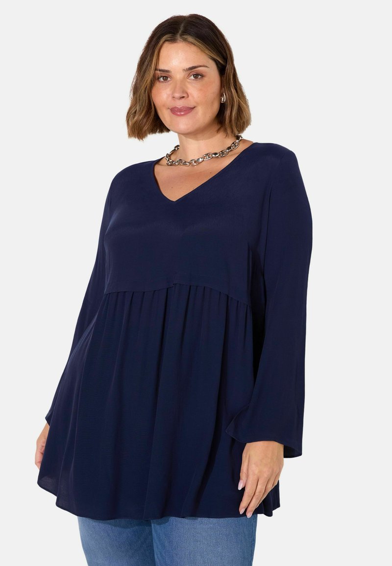 Mörkblå blus med V-ringning, långa klockärmar och rynkad detalj vid midjan, tillverkad av ett lättviktigt tyg.