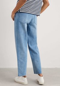Jeans en denim bleu clair avec une coupe décontractée, présentant des jambes droites et des poches arrière. L'ensemble est associé à des baskets blanches.