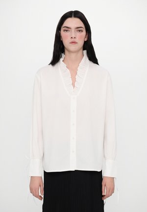 Weiße Bluse mit langen Ärmeln, Rüschenausschnitt, Knopfleiste und elastischen Bündchen. Aus leichtem Stoff mit glatter Textur hergestellt.