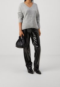 Maglione grigio a maglia con scollo a V e texture a coste, abbinato a pantaloni in ecopelle nera ad alta lucentezza e una piccola borsa nera.