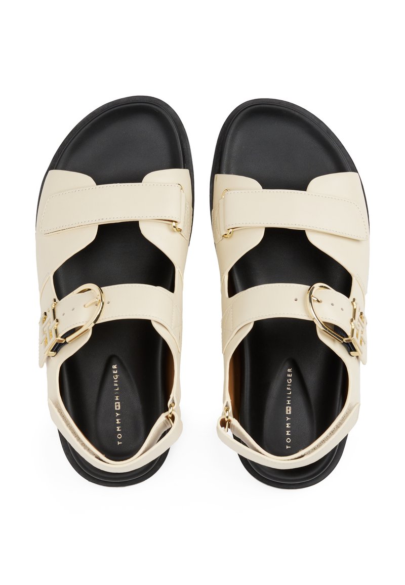 Beige Leder-Sandalen mit schwarzen Sohlen, ausgestattet mit verstellbaren Riemen und goldenen Hardware-Details. Offene Zehen-Design mit einer strukturierten Oberfläche.