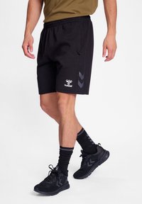 Schwarze Sportshorts aus einem Stoff mit glatter Textur, die an der Seite ein Logo und ein Chevron-Design in Dunkelgrau aufweisen.