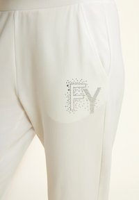 Joggers blancos y livianos con una textura suave, que presentan un logo "FY" decorado con cristales y bolsillos laterales.