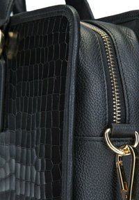 Zwarte leren tas met een geprofileerd krokodillenpatroon aan de ene kant, een gladde afwerking aan de andere kant, voorzien van gouden hardware en een ritsluiting.