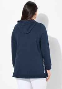 Felpa con cappuccio blu navy, maniche lunghe, spacchi laterali, scritta bianca "TRUE CASUAL" sul lato sinistro, tessuto morbido, design casual.
