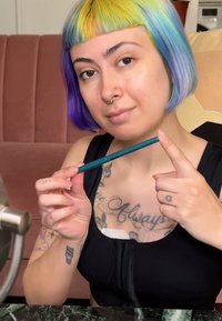 En turkos penna hållen i handen, med en vass spets och en jämn yta. I bakgrunden syns en rosa soffa och en spegelbild.