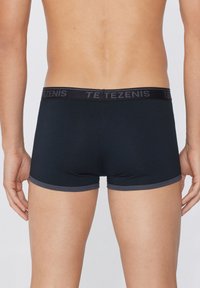 Schwarze Boxershorts mit einem grauen Bund, der mit "TEZENIS"-Branding versehen ist, aus glattem, dehnbarem Material gefertigt, mit einem figurnahen Design.