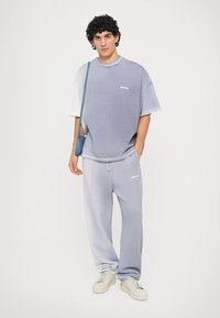Overdimensjonert lilla gradient t-skjorte med hvit logo, kombinert med matchende joggebukser og kremfargede sneakers. Glatt stoff og avslappet passform.