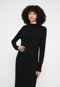 Fekete hosszú ujjú ruha puha anyagból, magas nyakkivágással és testhez simuló szabással, sima textúrával és látható minták nélkül.