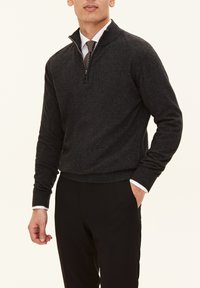 Dunkelgrauer Reißverschluss-Pullover aus weichem Stoff, mit hohem Kragen und gerippten Bündchen, kombiniert mit maßgeschneiderten schwarzen Hosen.